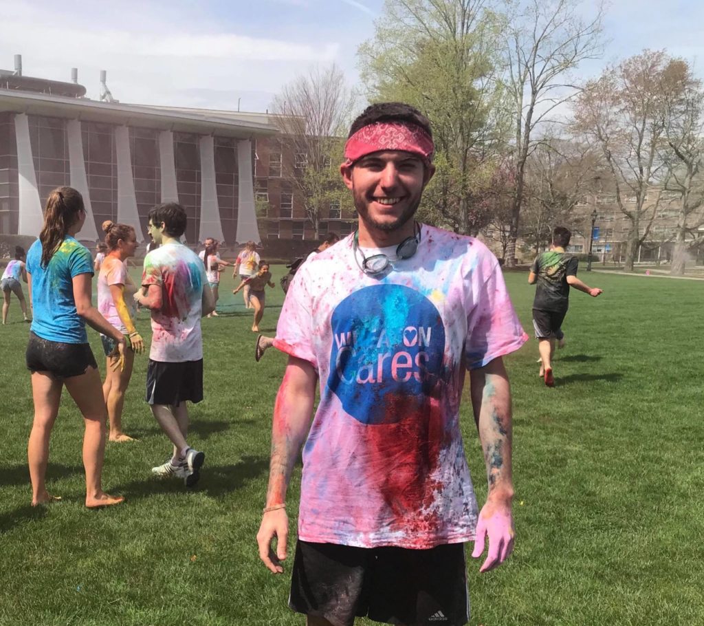 A photo of a man covered in colored powder and standing barefoot in the grass
