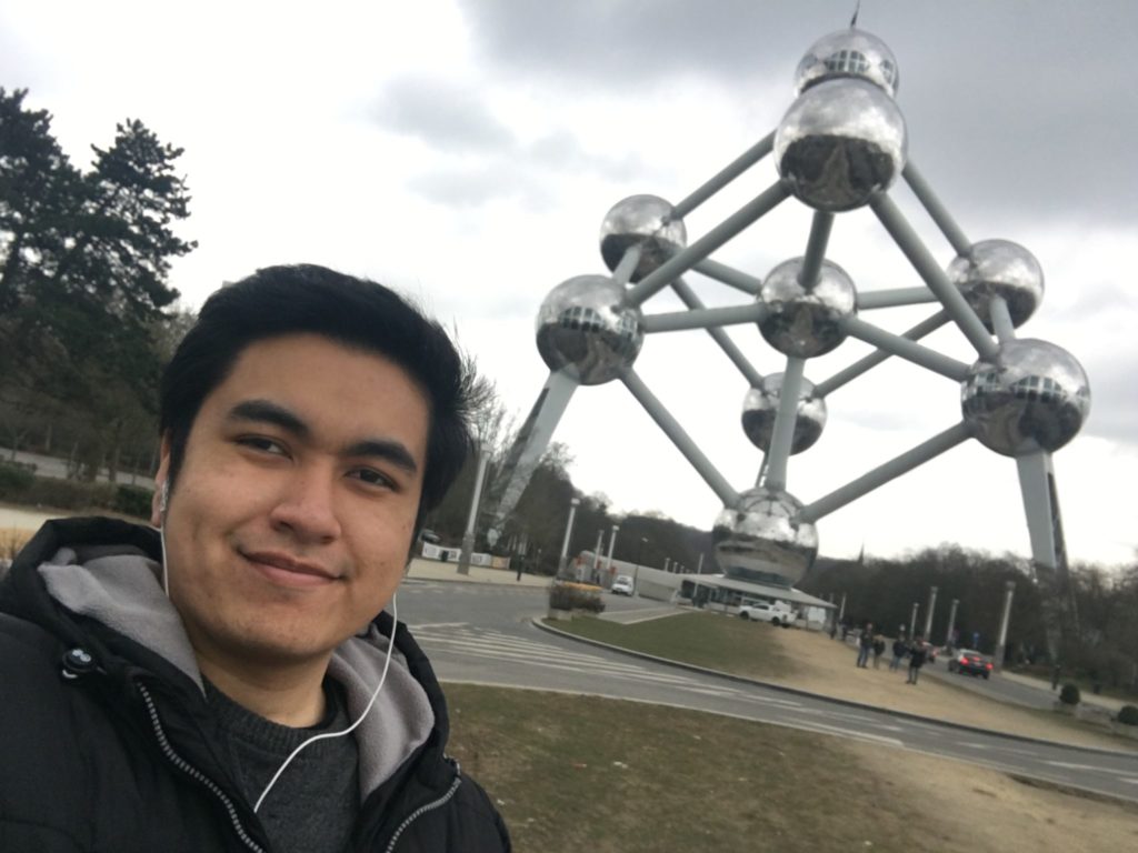 A photo of a man in front of a metallic structure connecting together via round circular objects.