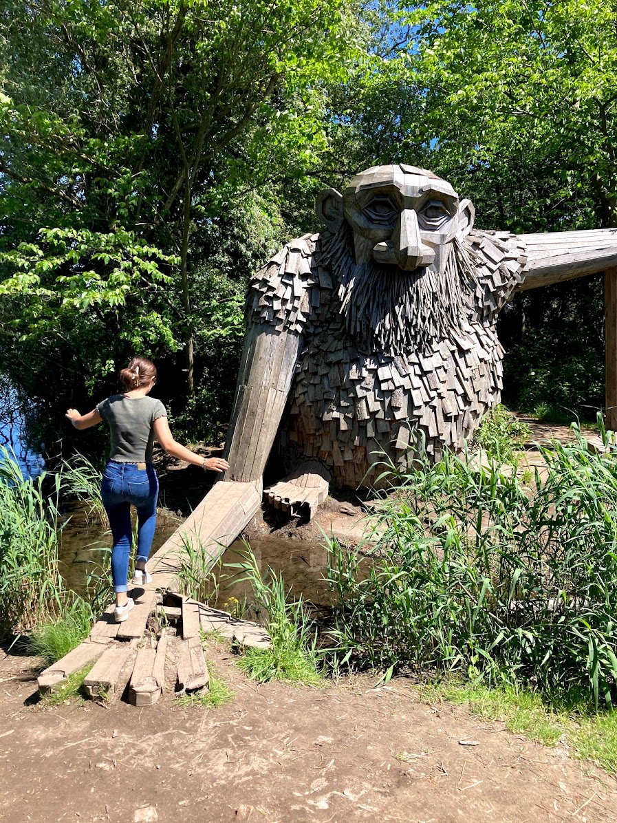 A student walks along a wooden board towards a large wooden troll statue in the Danish countryside 