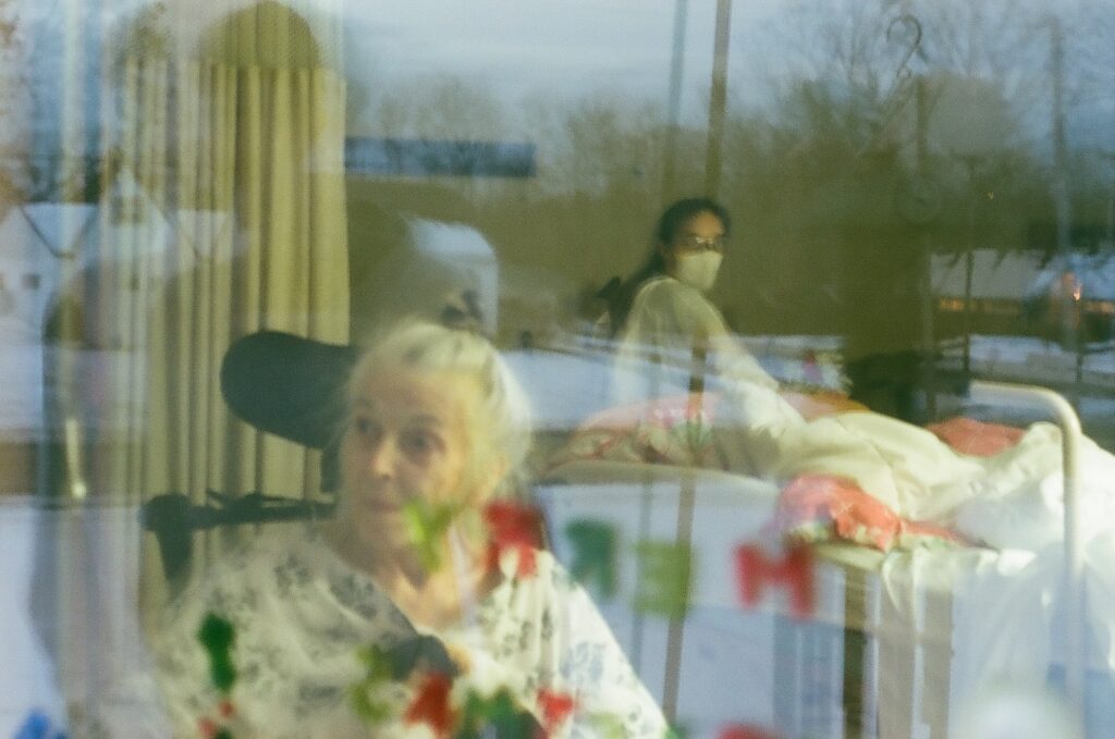 Captured on film, Carol Love spends Christmas looking out her window. Relatives spell "Merry Christmas" as she can not hear from the other side.
