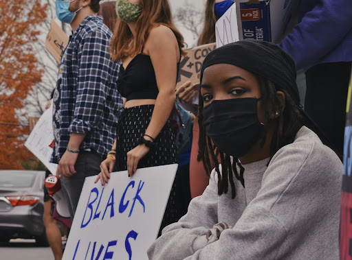 A masked student looks at the camera, with Black Lives Matters protests in the background.