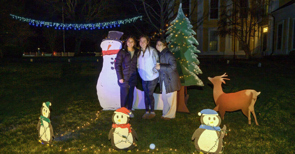 Three students posing with cardboard cutouts of a snowman, a deer and a Christmas tree